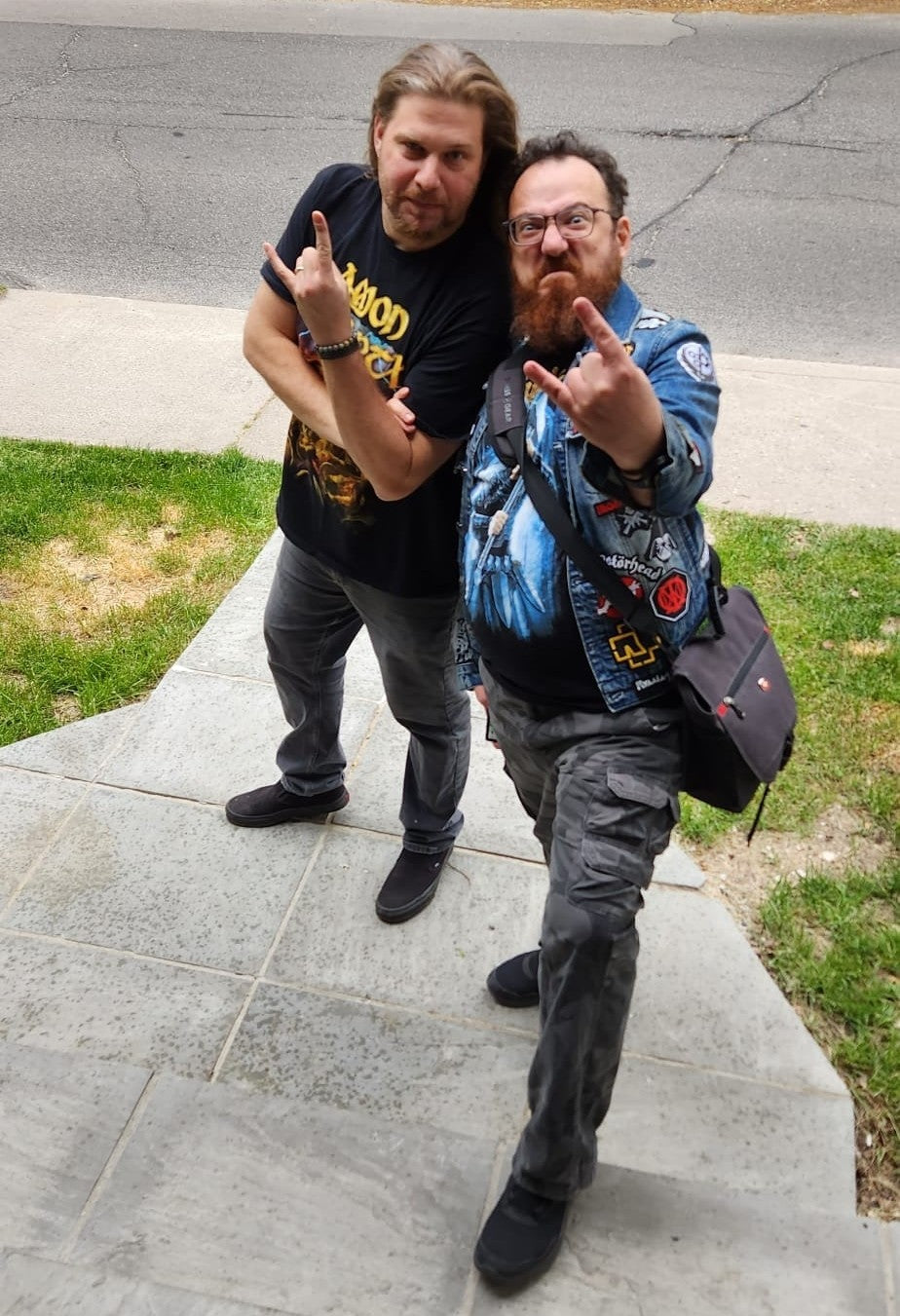 Two men posing on a sidewalk making horns up signs.